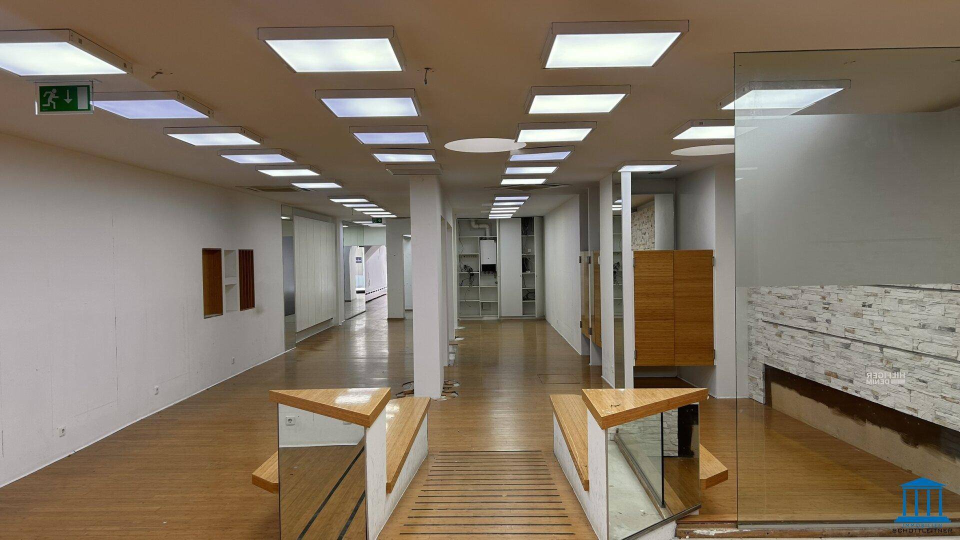 Großzügiger Verkaufsraum mit Holzfußboden, weißen Wänden und verschiedenen Präsentationselementen.