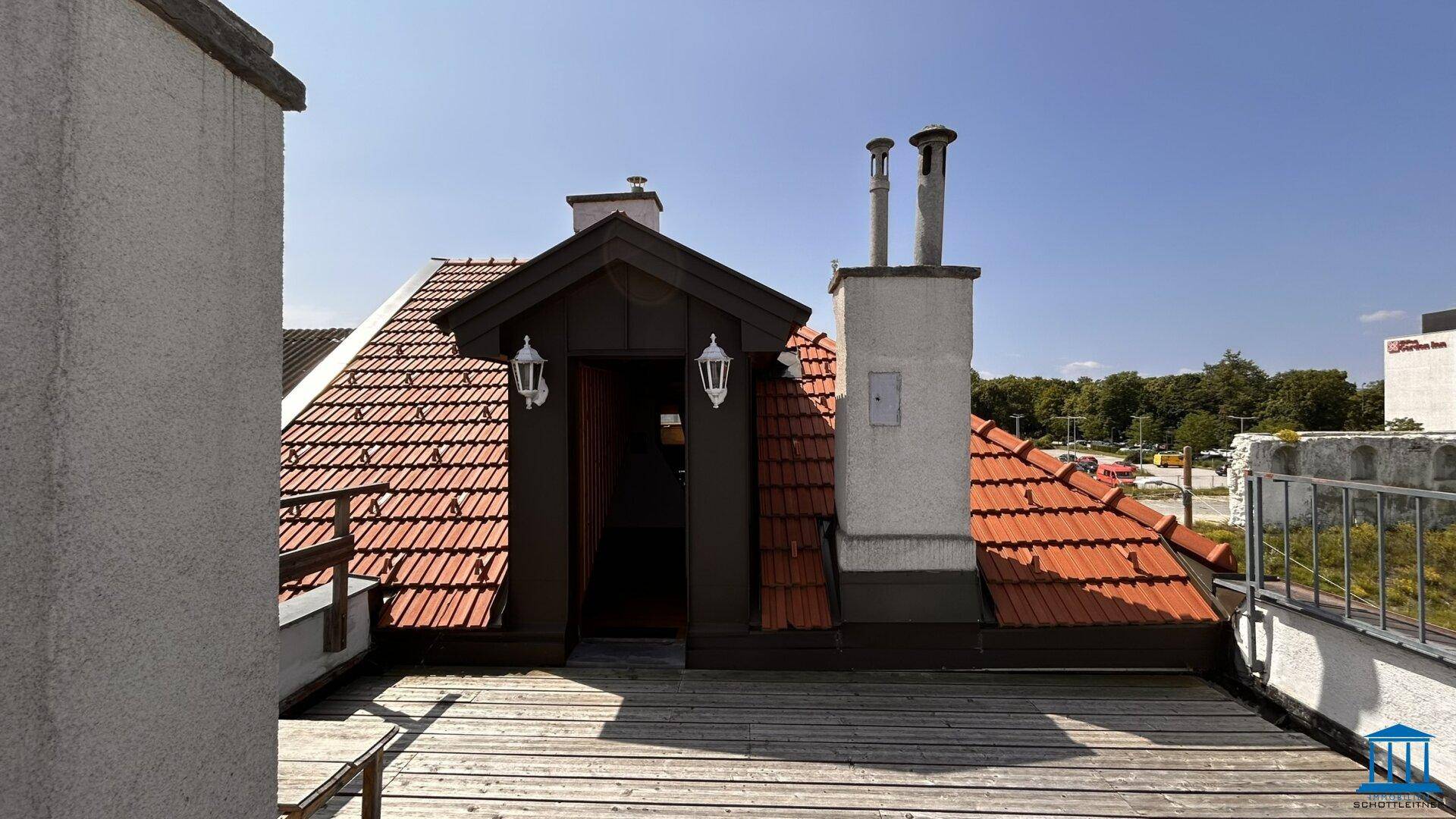 Geräumige Dachterrasse mit Holzboden, Ziegeldächern und einem kleinen Dachausbau mit Laternen und Schornsteinen.
