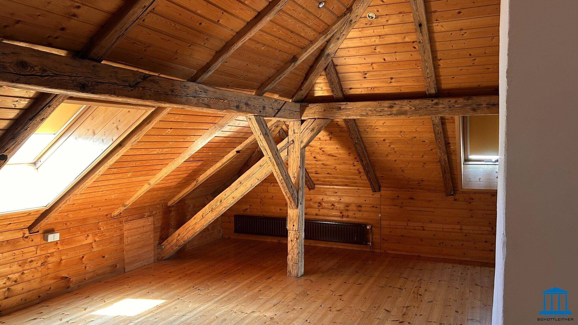 Geräumiger Dachboden mit Holzbalken, Holzverkleidung und Dachfenstern, die viel natürliches Licht hereinlassen.