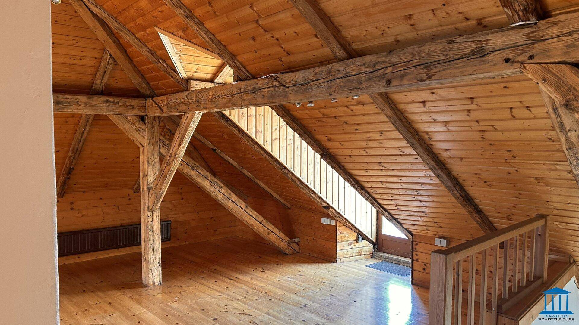 Großer Dachbodenraum mit sichtbaren Holzbalken, Holzverkleidung und Holzboden, hell durch Dachfenster.