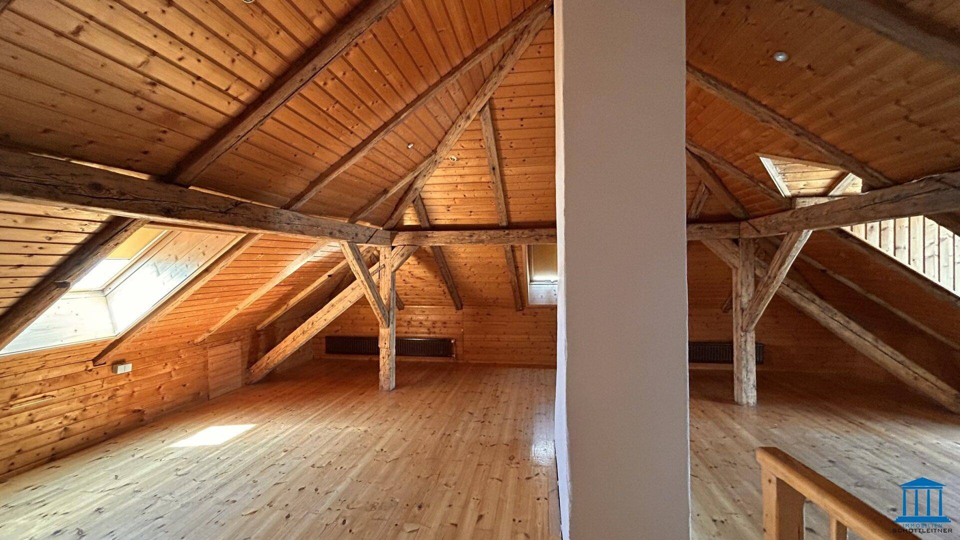 Heller Dachbodenraum mit sichtbaren Holzbalken, Holzverkleidung und Holzboden, ideal für Ausbau.