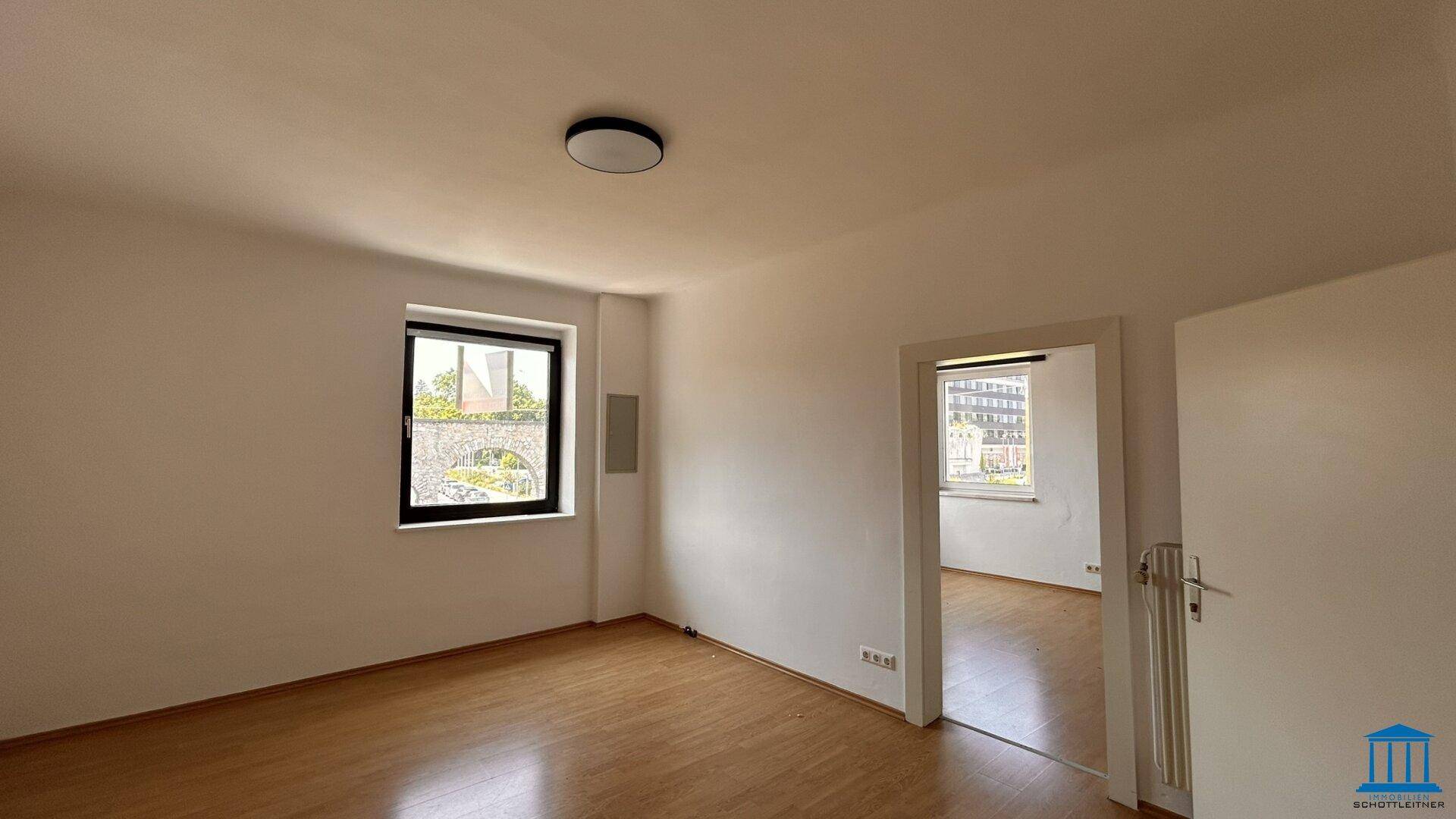Heller Raum mit Holzboden, weißen Wänden und zwei Fenstern, die viel Tageslicht bieten.
