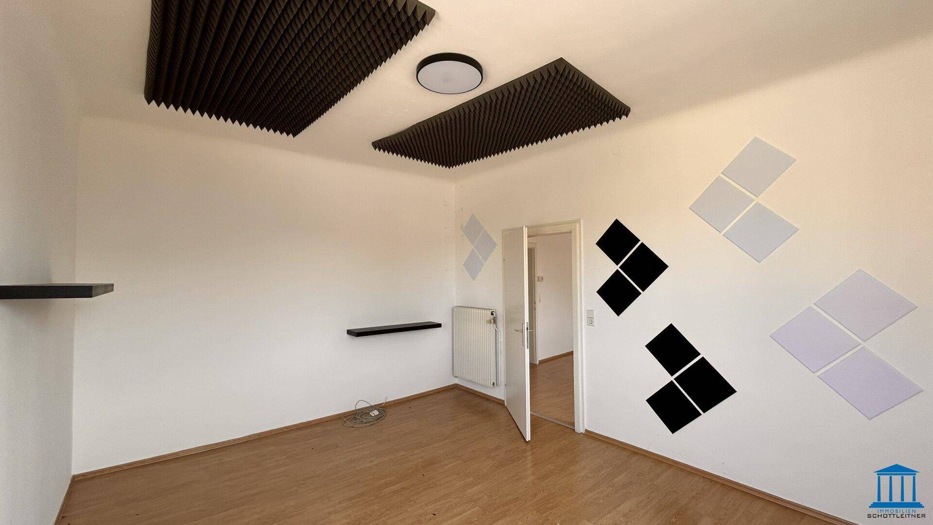 Heller Raum mit Holzboden, weißen Wänden und Akustikpaneelen an Decke und Wänden.