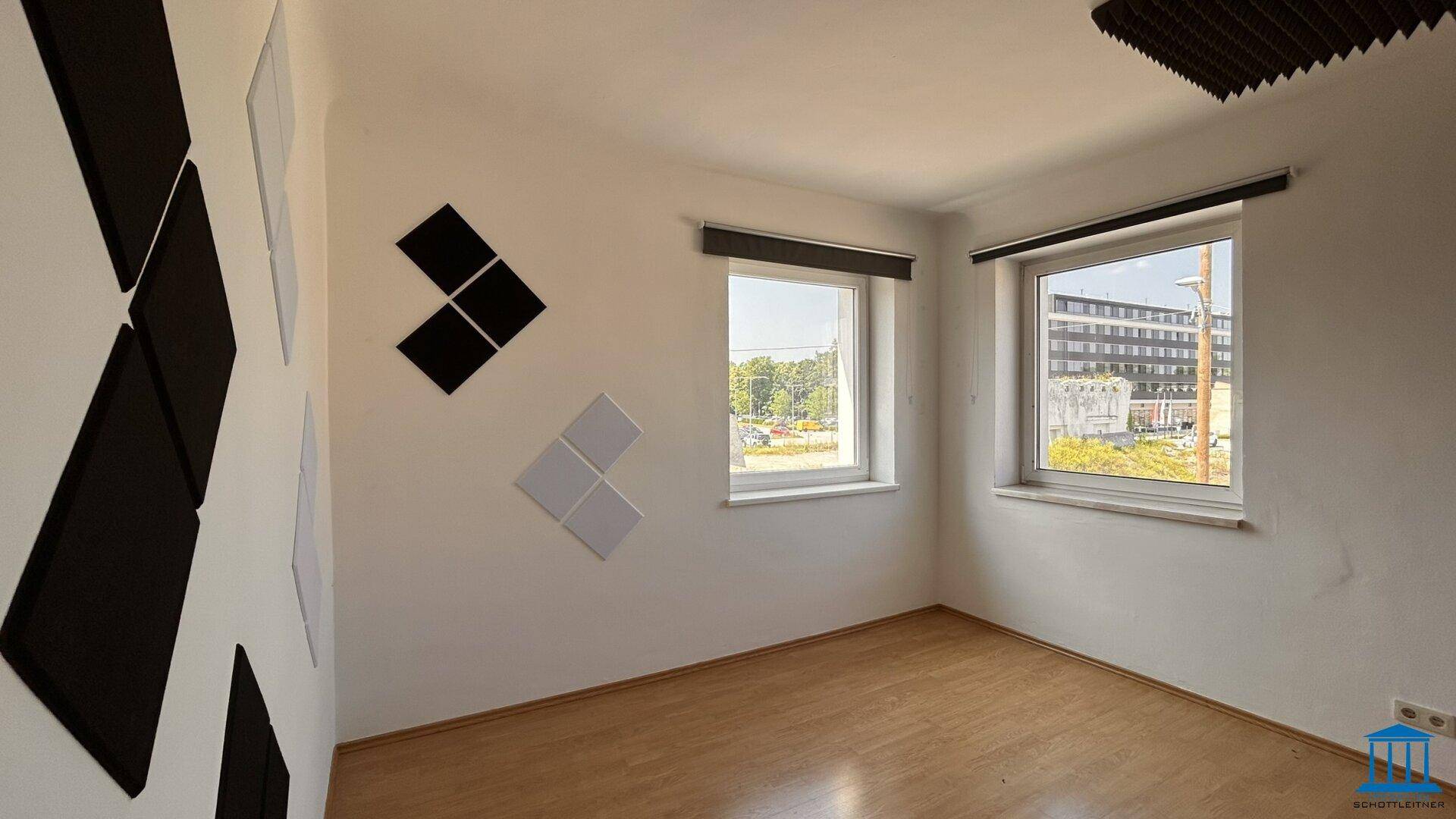 Raum mit Holzboden, weißen Wänden und schwarzen sowie weißen Akustikpaneelen an den Wänden.