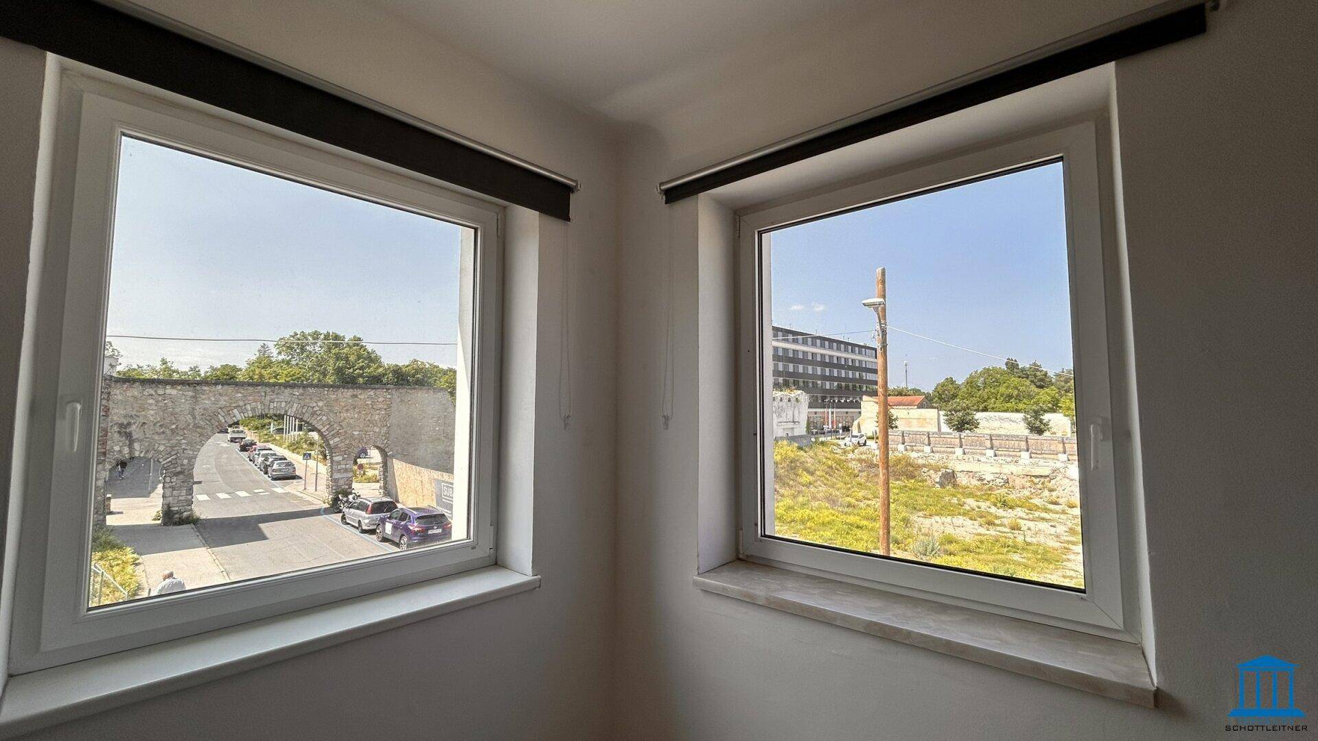 Fenster mit Blick auf eine historische Steinbrücke und eine ländliche Umgebung mit Bäumen und Feldern.