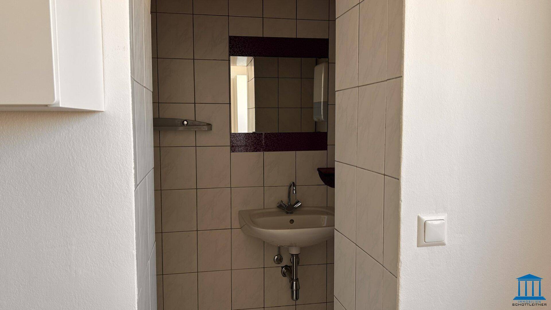 Kleiner Badezimmerbereich mit Waschbecken, Spiegel und Fliesen an den Wänden.