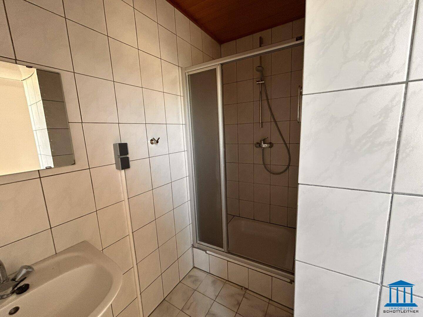 Gefliestes Badezimmer mit Duschkabine, Waschbecken und Spiegel, in gutem Zustand.