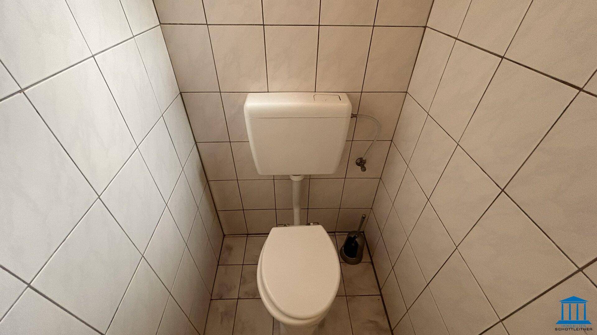 Toilettenraum mit weißer Keramik und hellen Fliesen an Wänden und Boden.