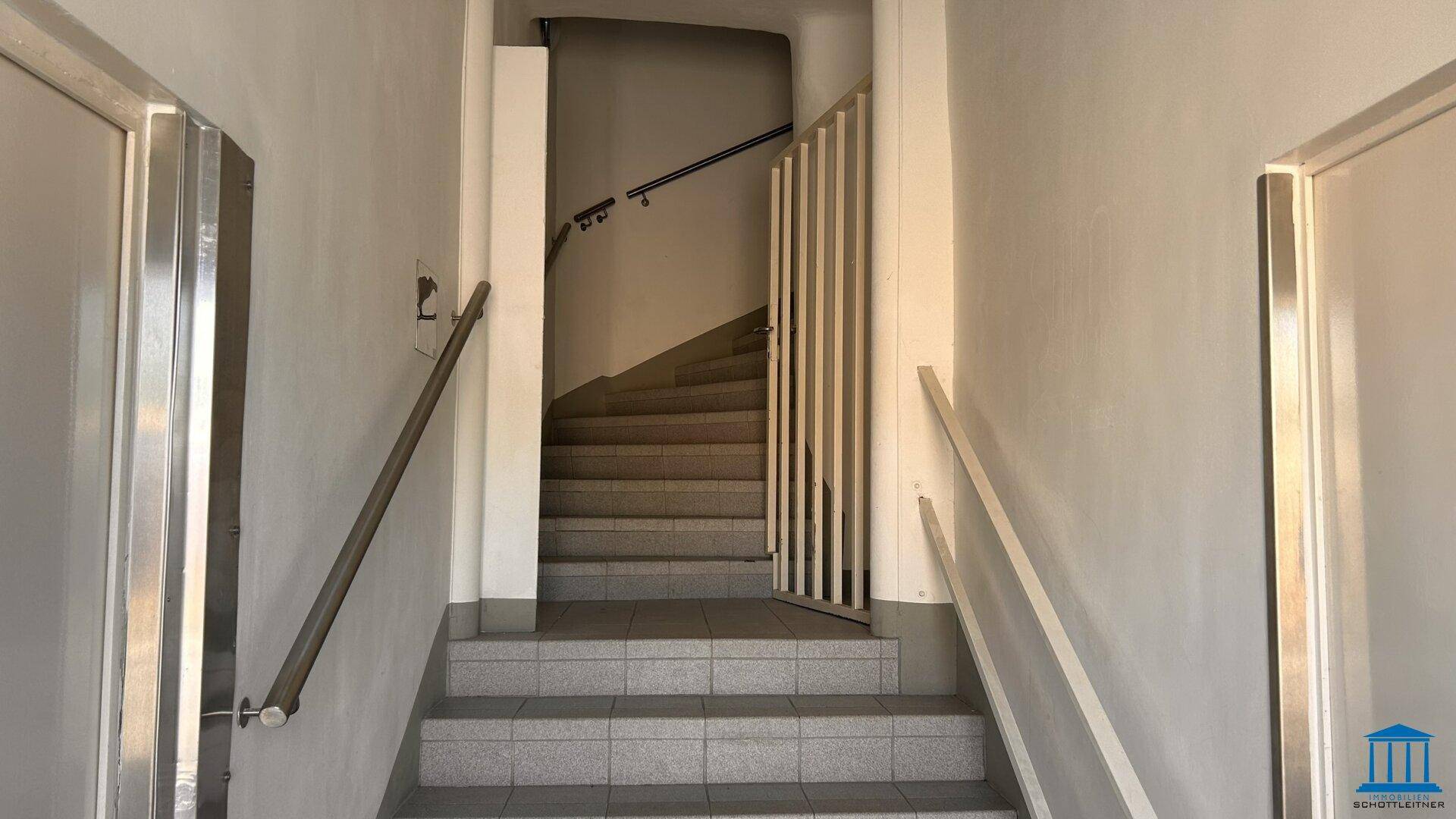 Helles Treppenhaus mit gefliesten Stufen, Geländer und Handläufen, die zu den oberen Etagen führen.