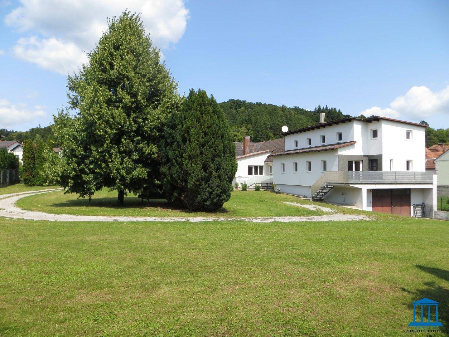 Großzügiger Gartenbereich mit Rasenfläche, Bäumen und Blick auf das Wohnhaus mit Balkon.