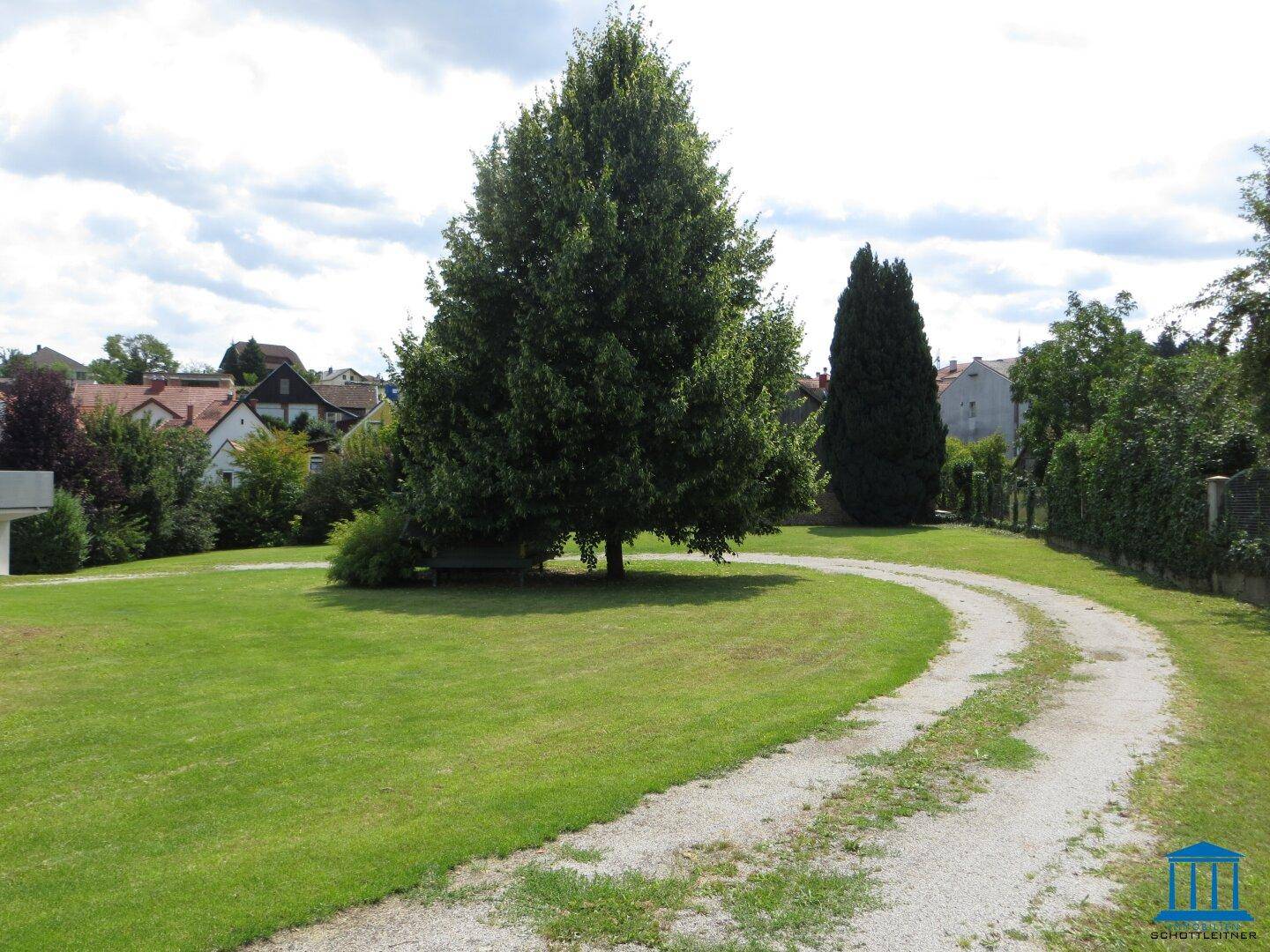 Weitläufiger Garten mit geschwungenem Kiesweg, großen Bäumen und Blick auf die Nachbarschaft.