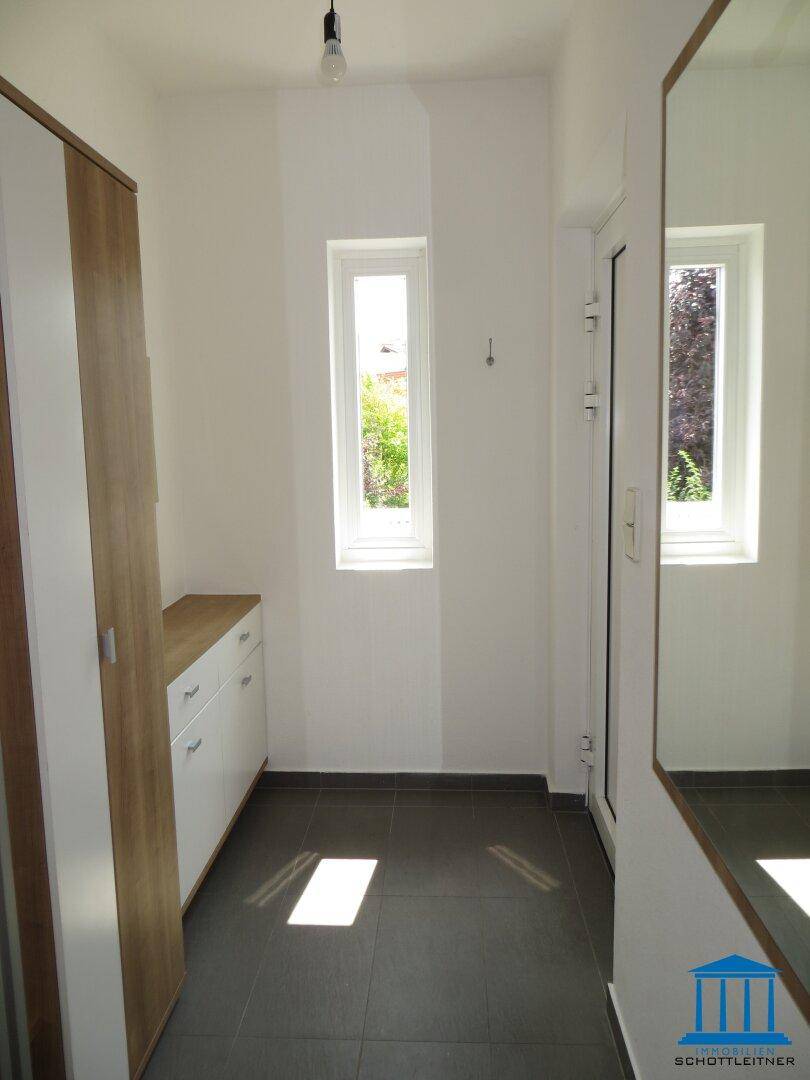 Heller Eingangsbereich mit Fliesenboden, schmalen Fenstern und einem Spiegelschrank.