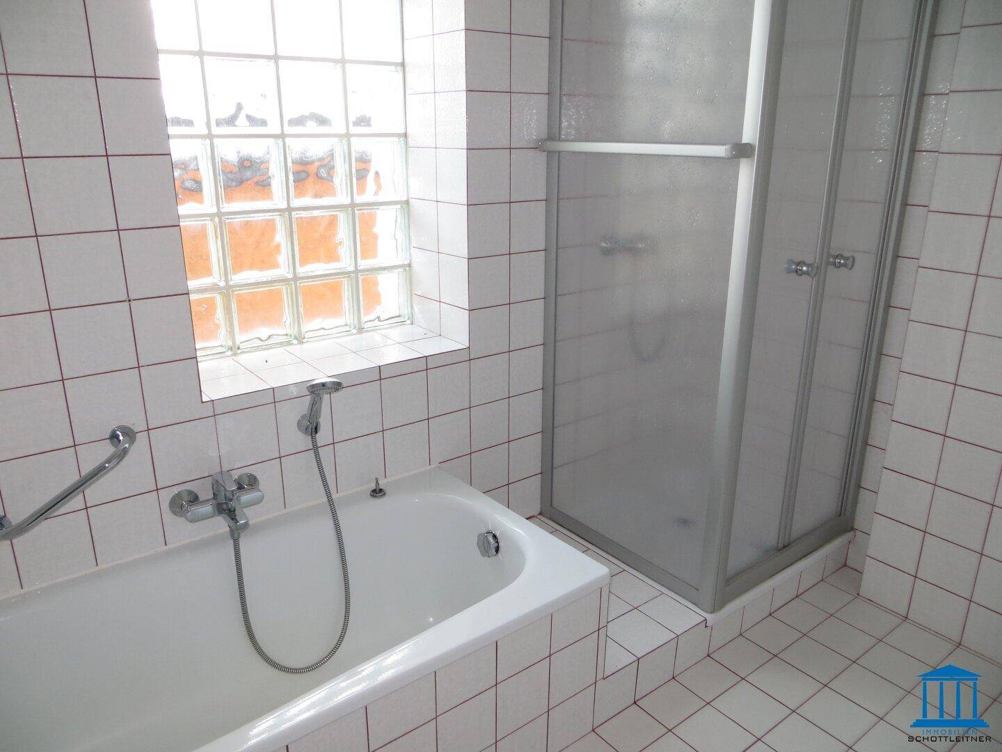 Gefliestes Badezimmer mit Badewanne, Duschkabine und Fenster aus Glasbausteinen.