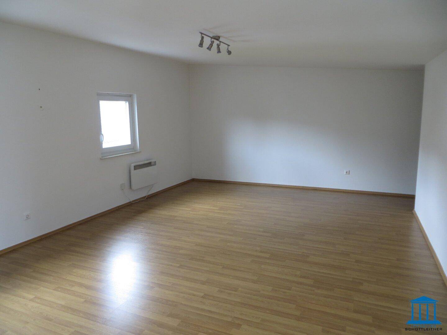 Helles Wohnzimmer mit Parkettboden und einem Fenster, das viel Tageslicht hereinlässt.