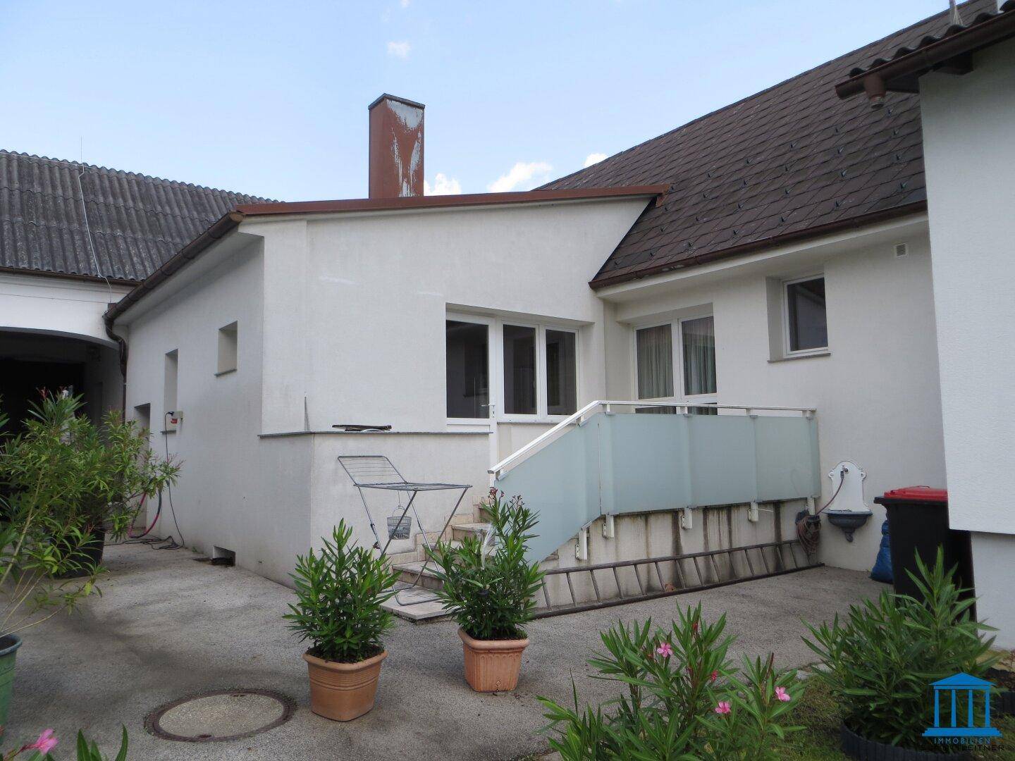 Kleine Terrasse mit Metalltisch und Stühlen, umgeben von Topfpflanzen.