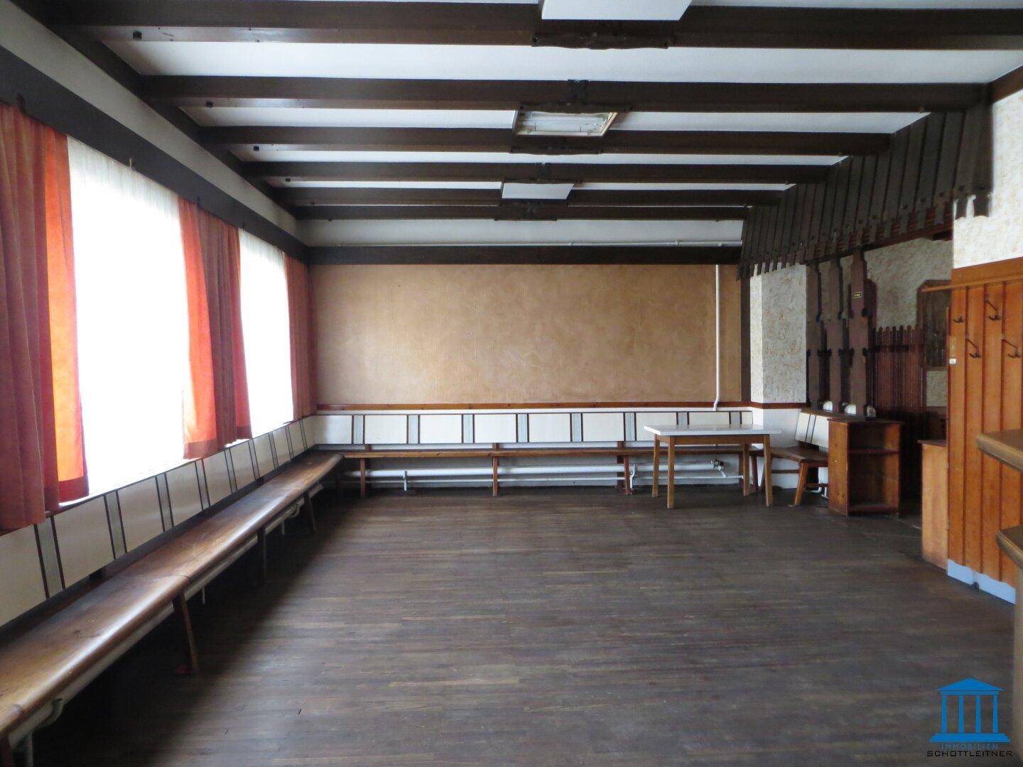 Geräumiger Raum mit Holzbalken, langen Holzbänken und dunklem Holzboden.