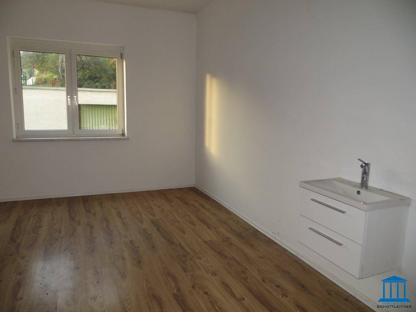 Funktionaler Raum mit Laminatboden, Fenster und einem kleinen Waschbecken mit Unterschrank.