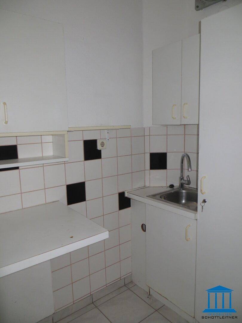Kleine, einfache Küchenzeile mit weißen Schränken, Spüle und gefliestem Fliesenspiegel, die Renovierung benötigt.