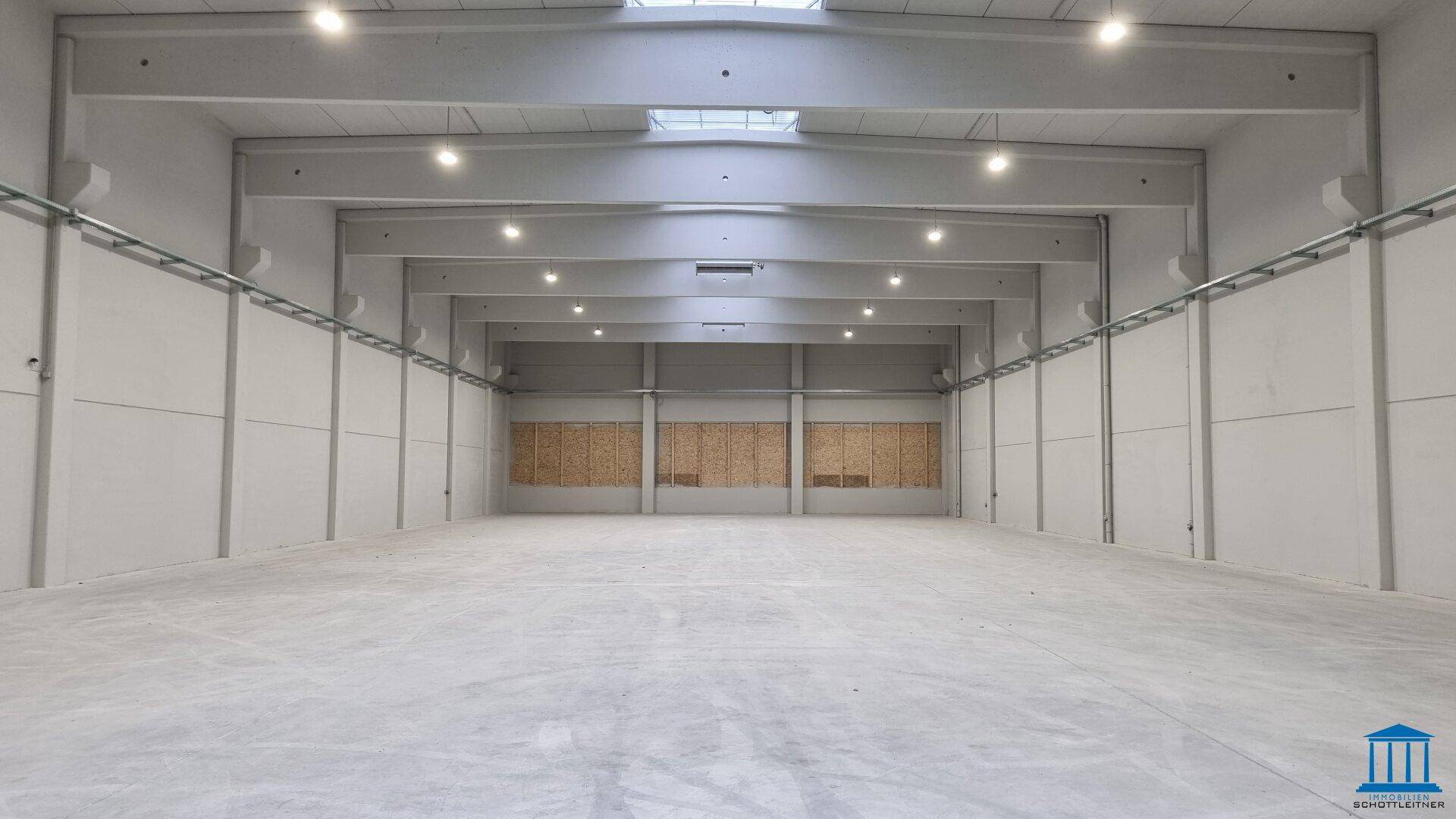 Weitläufige, leere Lagerhalle mit hohen Decken, Betonboden und Oberlichtern.