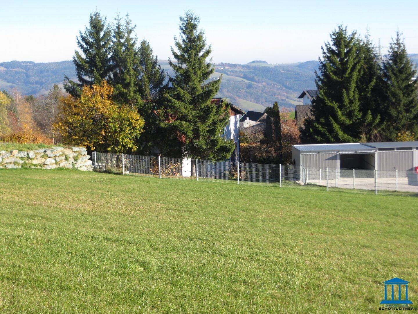 Offene Grünfläche mit Blick auf die Umgebung, Häuser und einen Carport am rechten Bildrand.