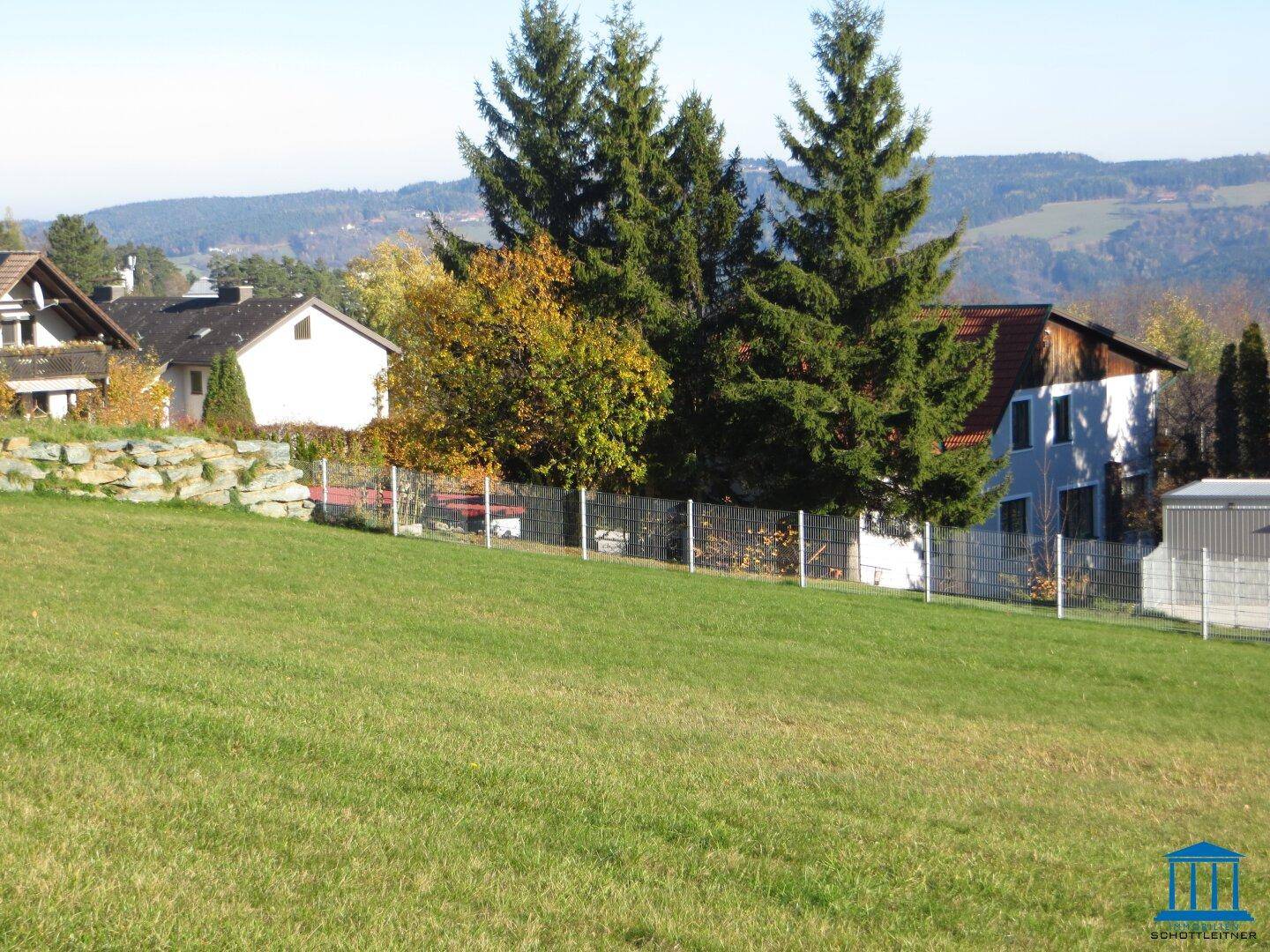 Sonnige Grünfläche mit Blick auf die Nachbarschaft und bewaldete Hügel im Hintergrund.