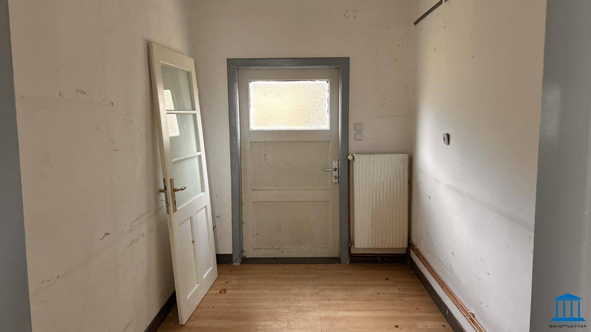 Kleiner Raum mit Holzfußboden und zwei Türen, der eine Renovierung benötigt.