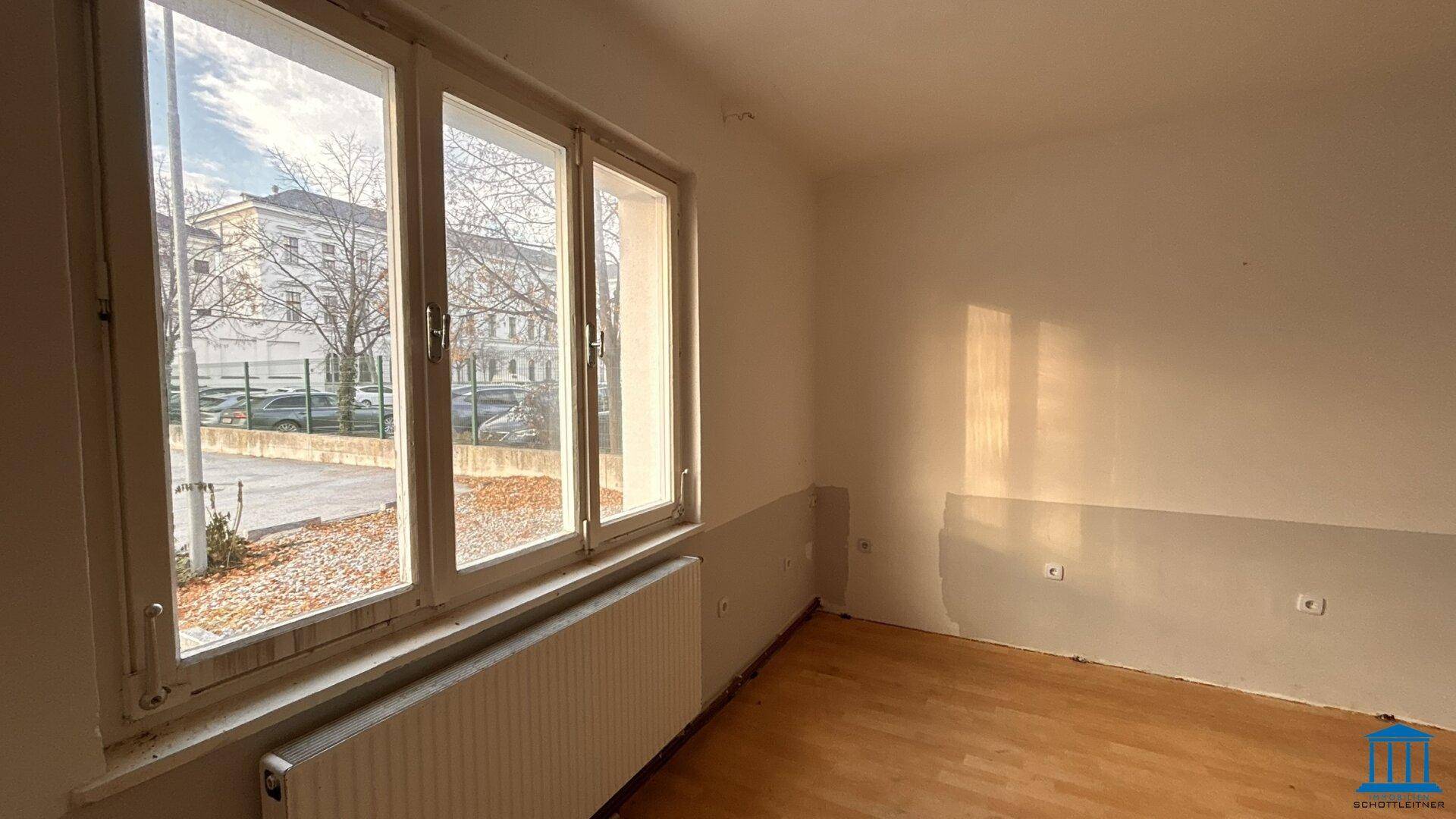 Leerer Raum mit Holzfußboden und einem großen Fenster, das den Blick auf die Umgebung freigibt.