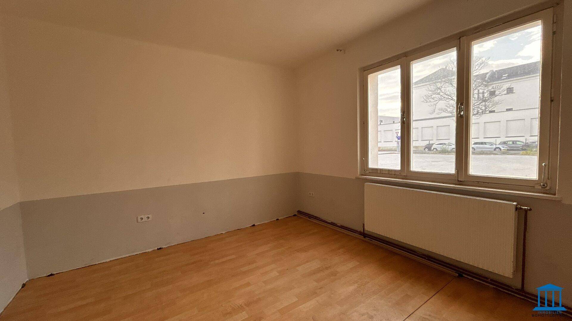 Leerer Raum mit Holzfußboden und einem großen Fenster, das den Blick auf die Umgebung freigibt.