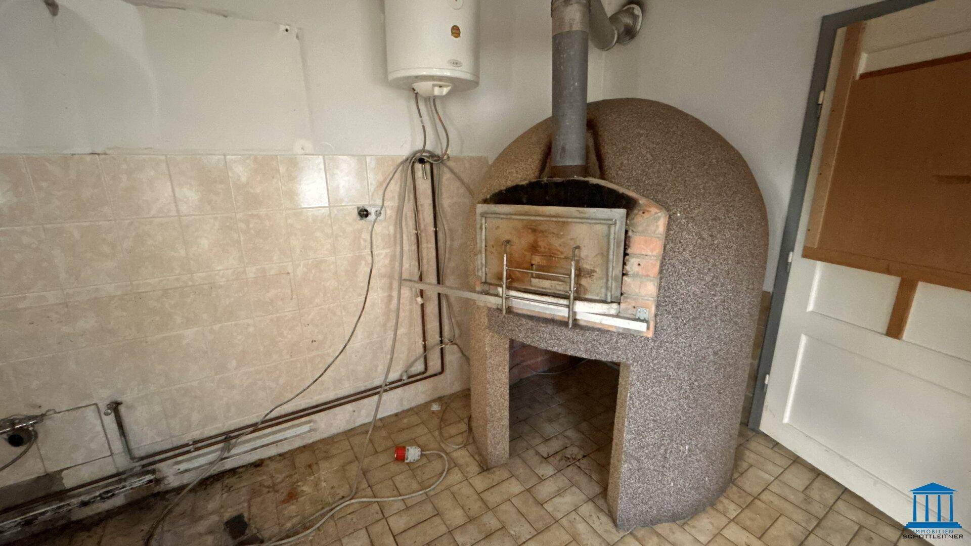 Raum mit einem großen, gemauerten Ofen und gefliesten Wänden, der eine Renovierung benötigt.