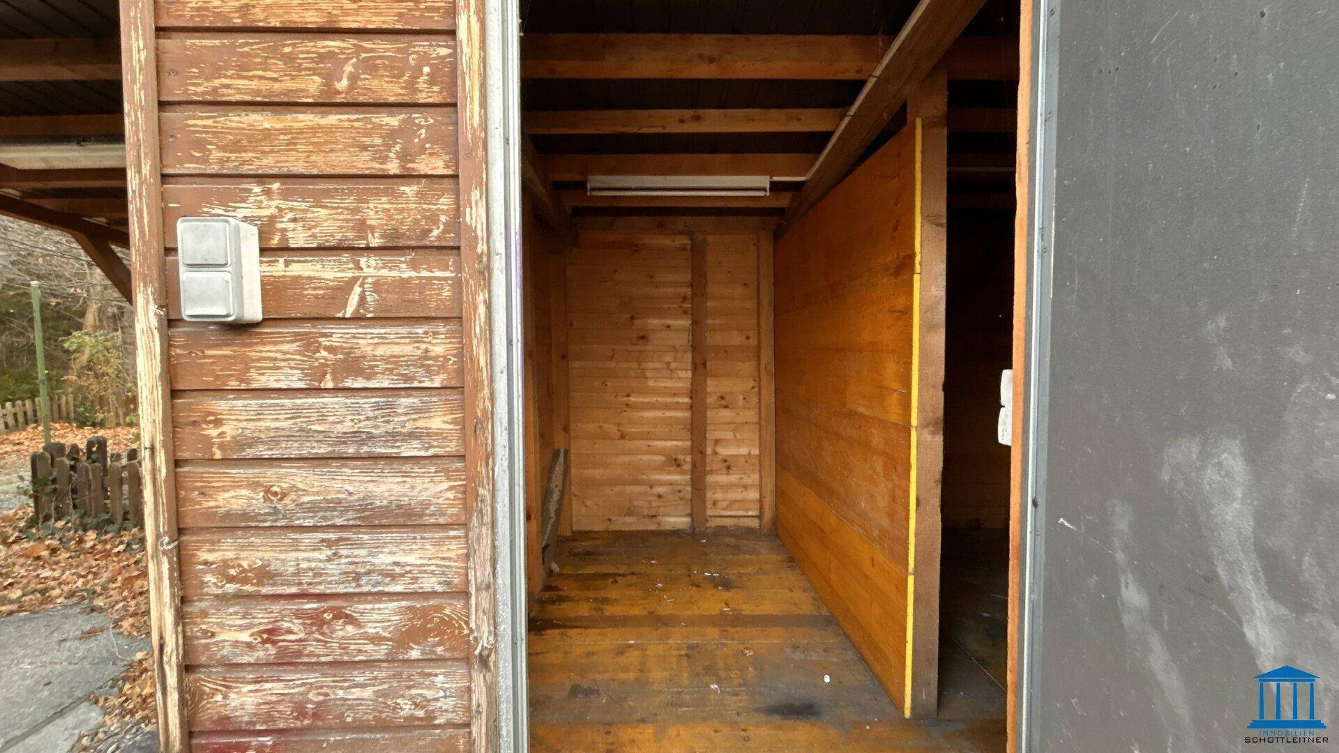 Innenansicht eines Holzschuppens mit sichtbaren Holzbrettern und einfacher Beleuchtung.