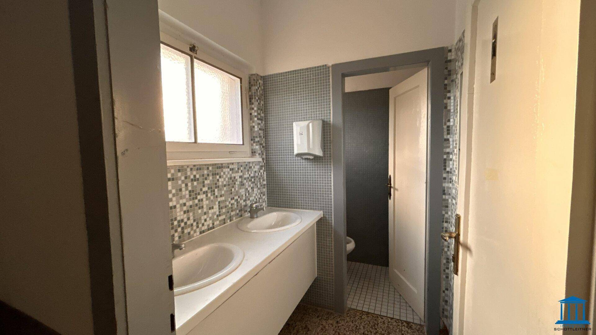 Badezimmer mit zwei Waschbecken, Mosaikfliesen und einem Fenster, das Tageslicht spendet.