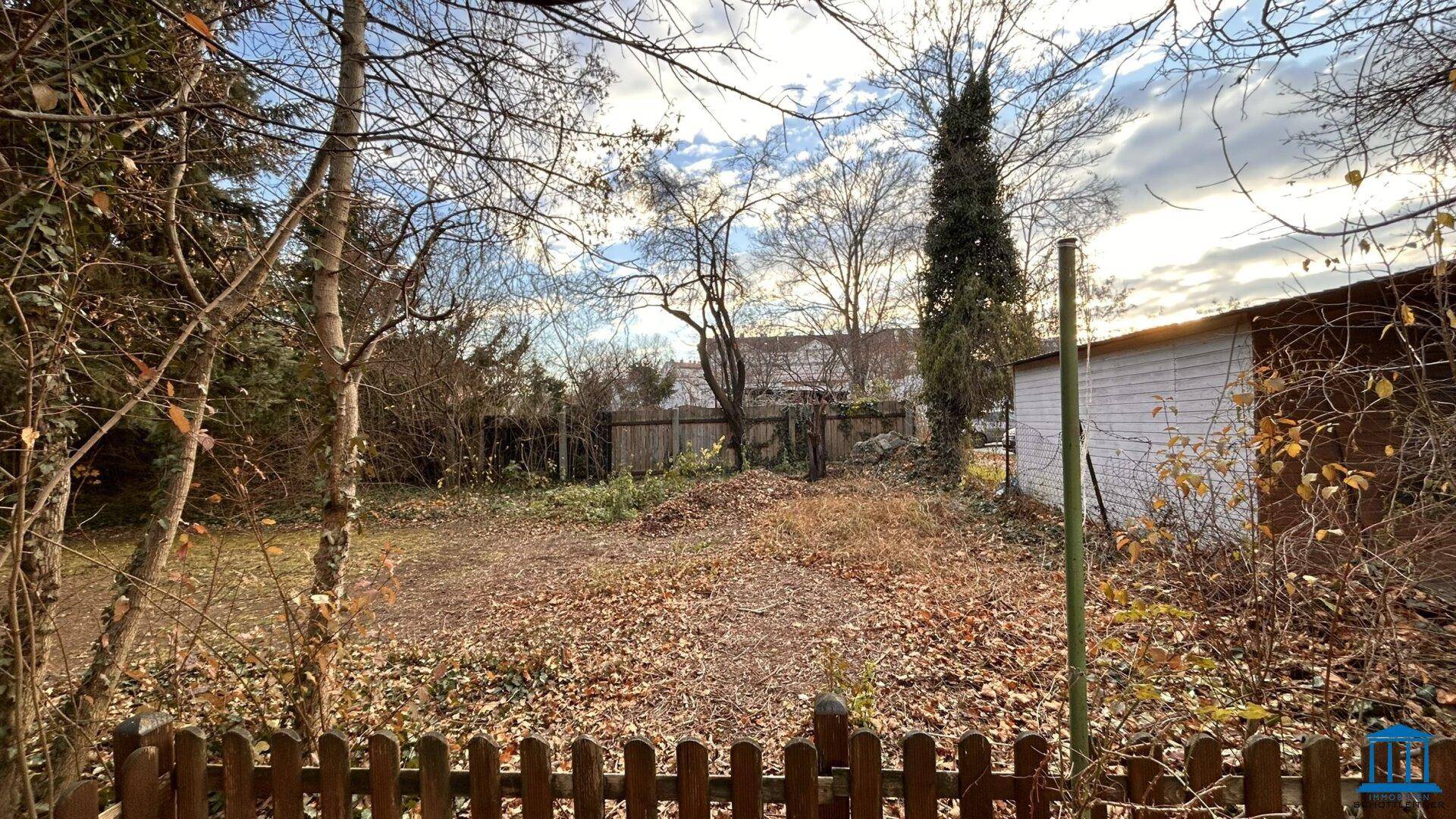 Gartenbereich mit Bäumen, Sträuchern und einem kleinen Schuppen im Hintergrund.