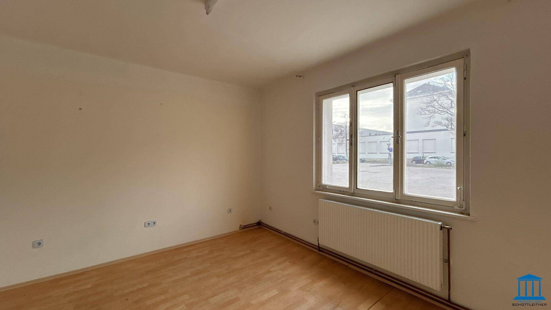 Leerer Raum mit Holzfußboden und einem großen Fenster, das den Blick auf die Umgebung freigibt.