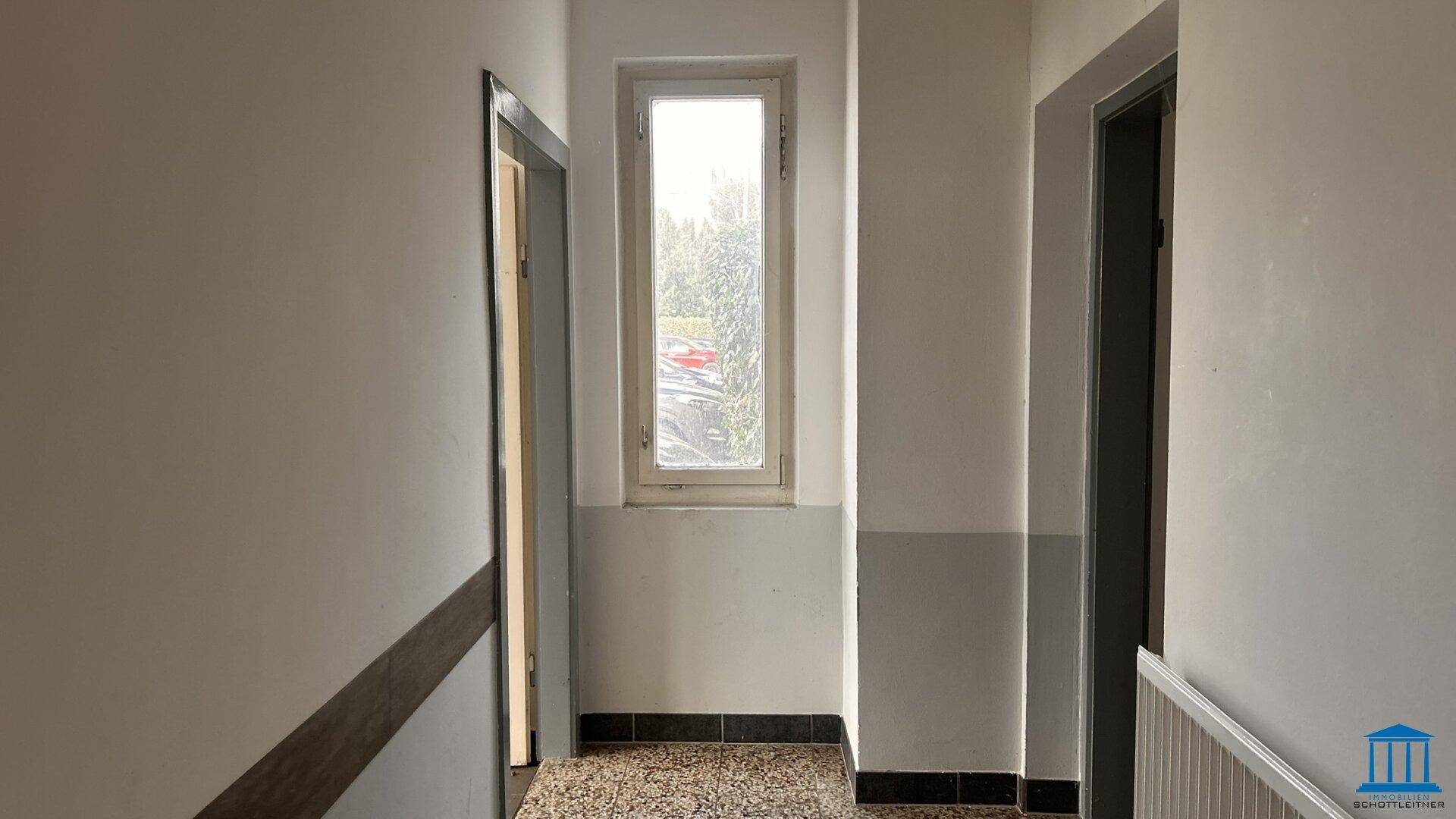 Heller Flur mit Terrazzoboden und einem hohen Fenster, das viel Tageslicht hereinlässt.