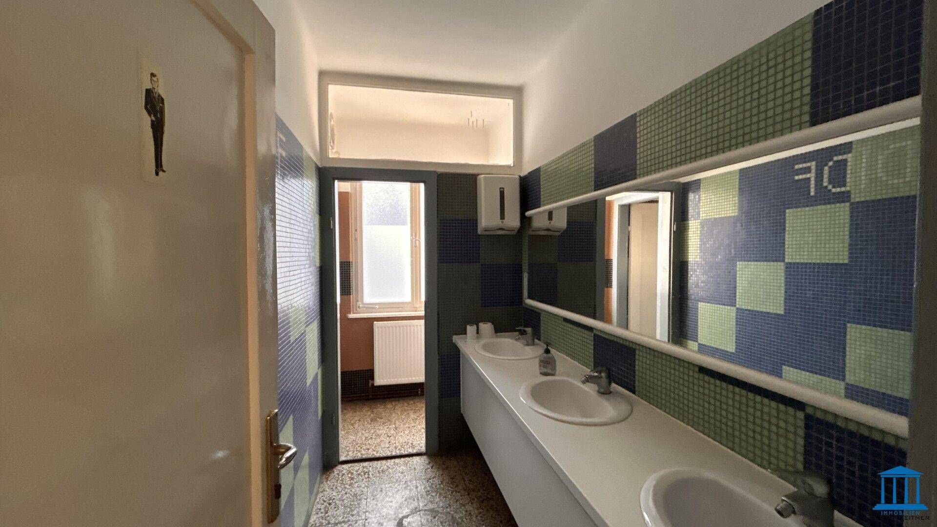 Badezimmer mit mehreren Waschbecken, Spiegeln und farbigen Mosaikfliesen an den Wänden.