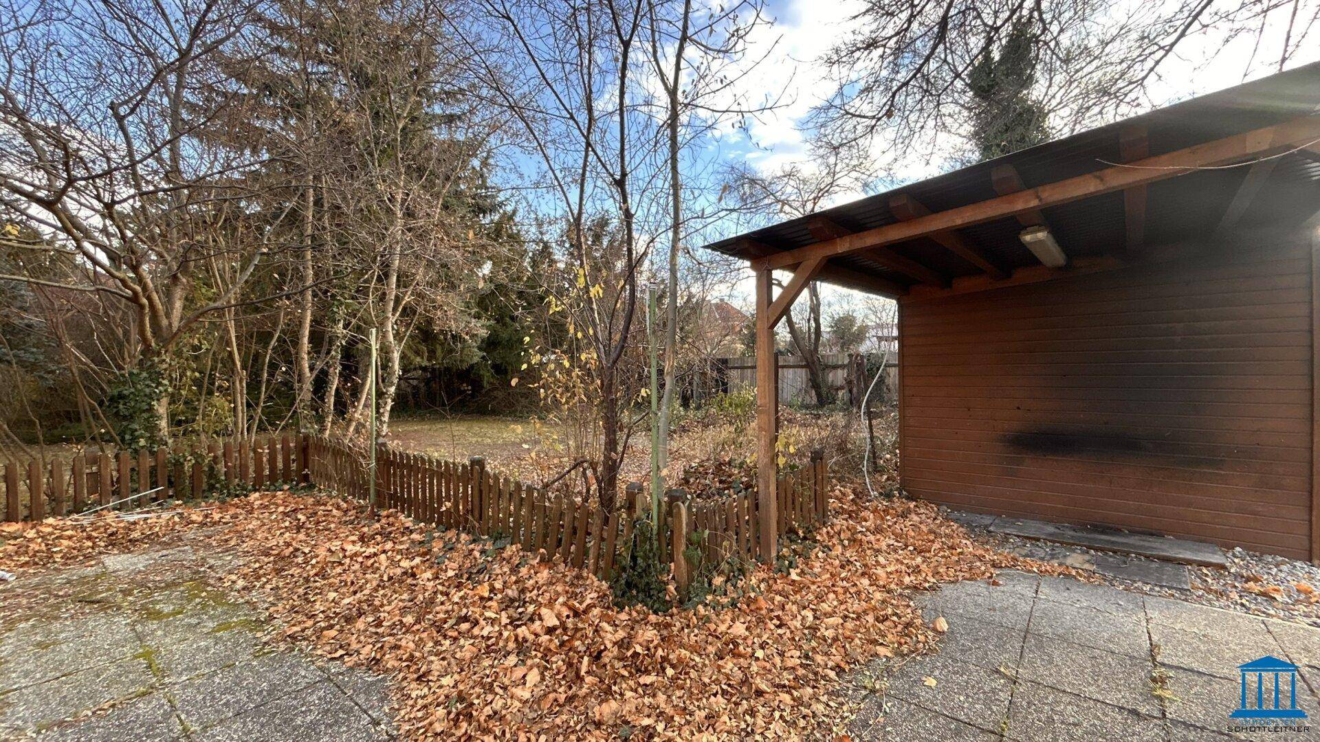 Überdachter Bereich mit Holzkonstruktion und einem Holzschuppen im Garten.