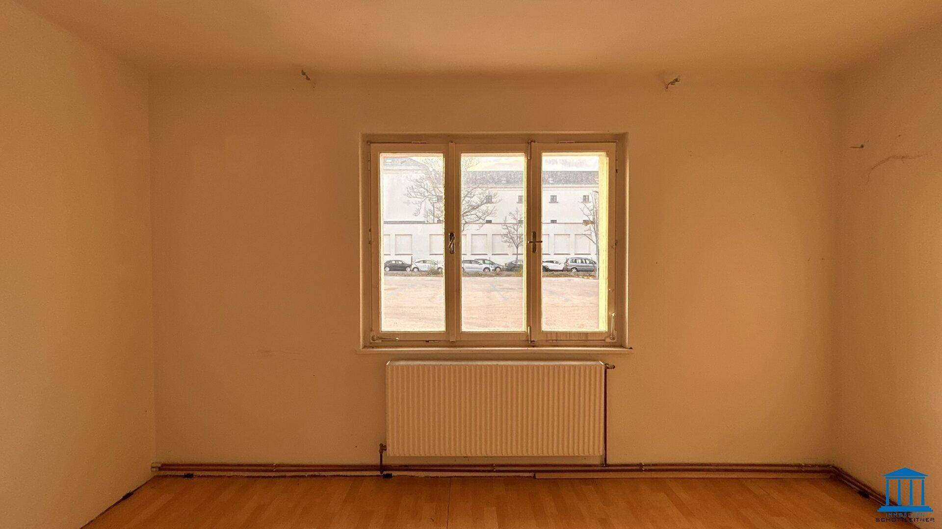 Leerer Raum mit Holzfußboden und einem großen Fenster, das den Blick auf die Straße ermöglicht.