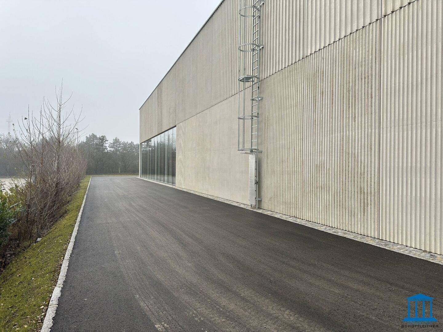 Seitenansicht eines modernen Industriegebäudes mit einer langen Zufahrt und einer Außenleiter.