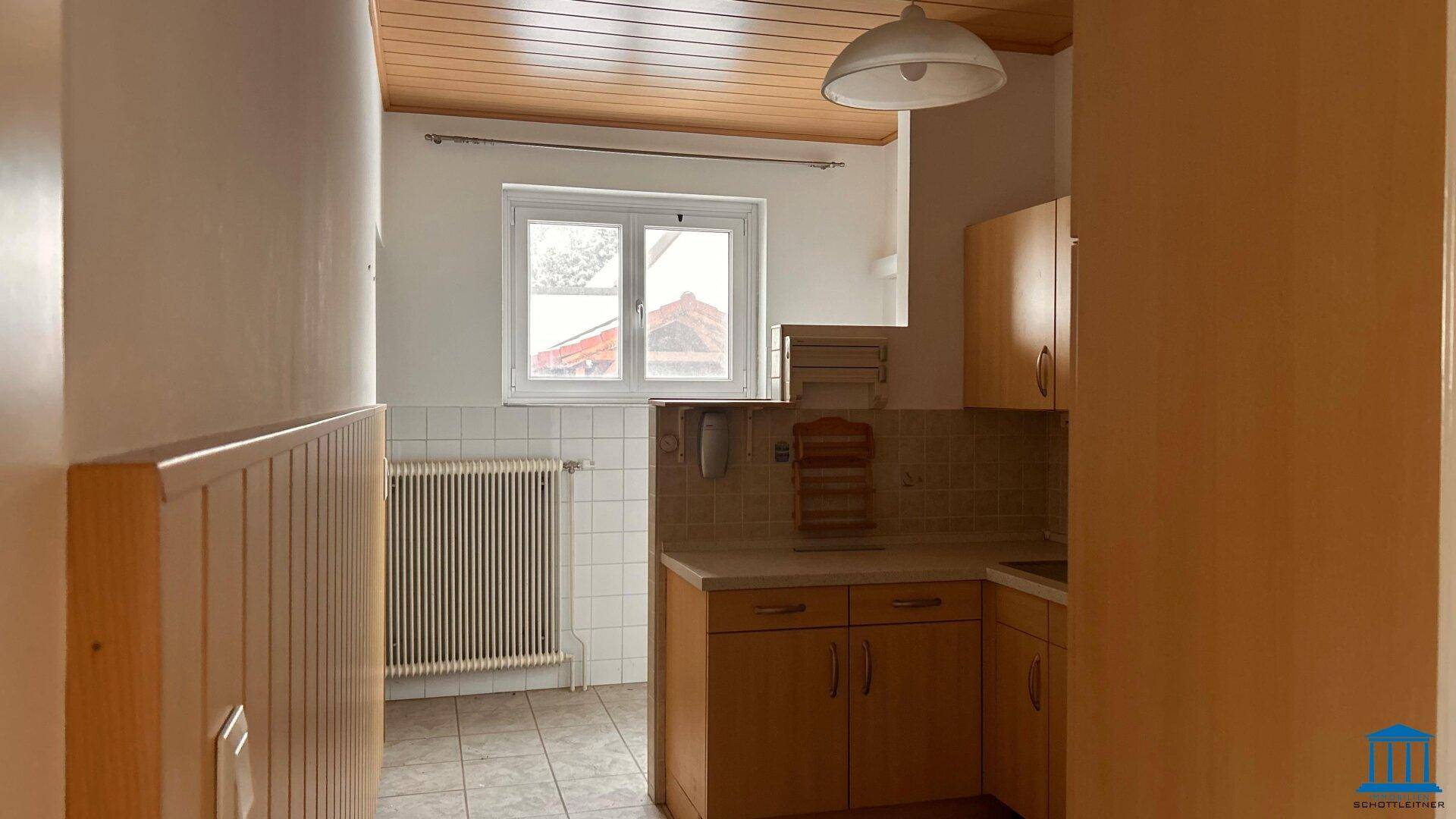 Helle Küche mit Holzdecke, Fliesenboden und einem Fenster mit Blick nach draußen.