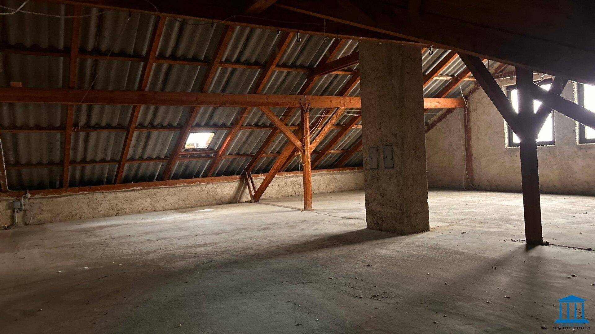 Geräumiger, unfertiger Dachboden mit sichtbaren Holzbalken und Dachfenster.