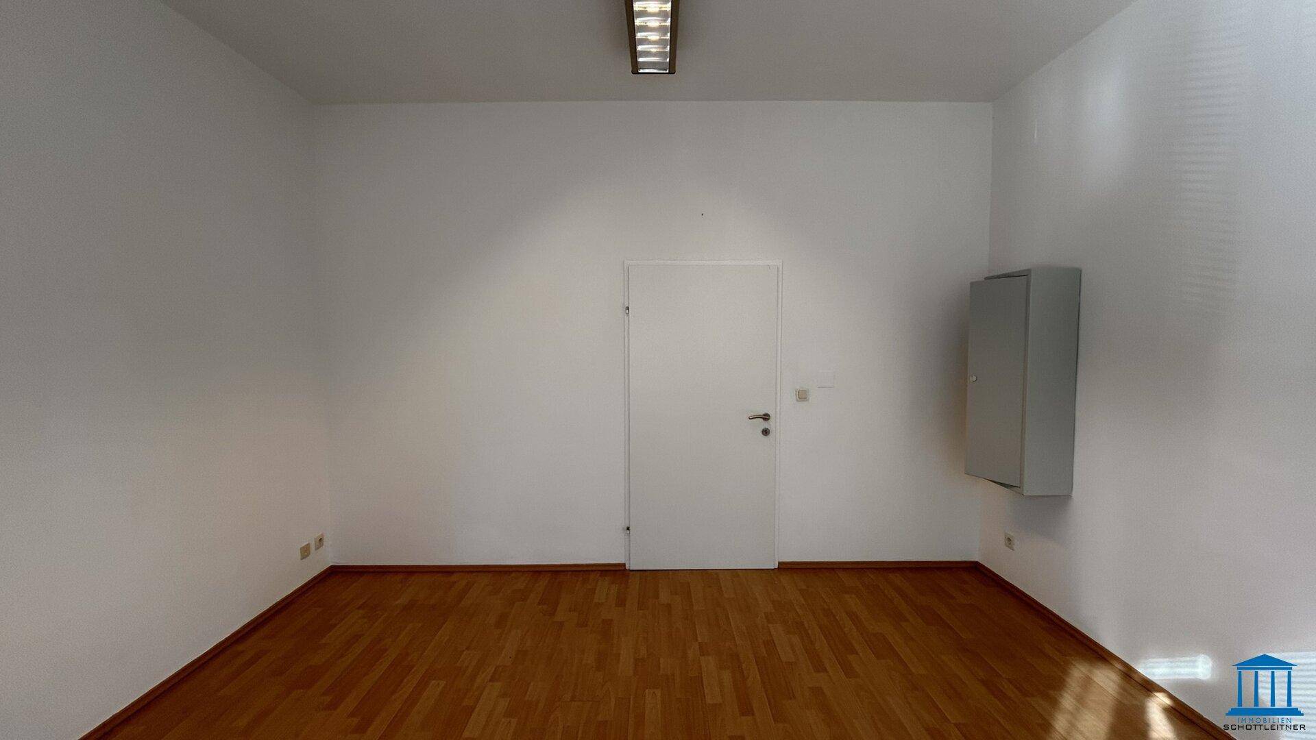 Leerer Büroraum mit weiß gestrichenen Wänden, Holzboden und einem Wandschrank.