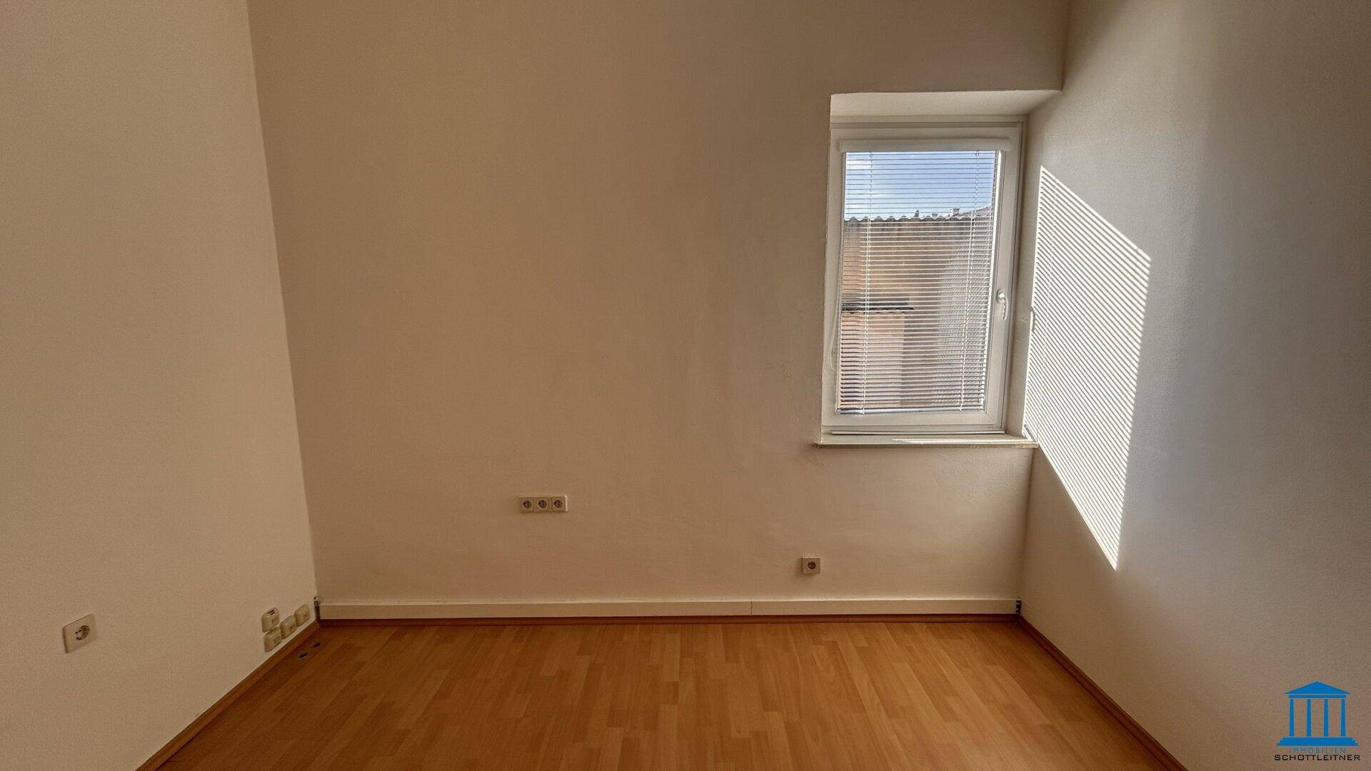 Kleiner Büroraum mit einem Fenster, das natürliches Licht hereinlässt, und Holzboden.