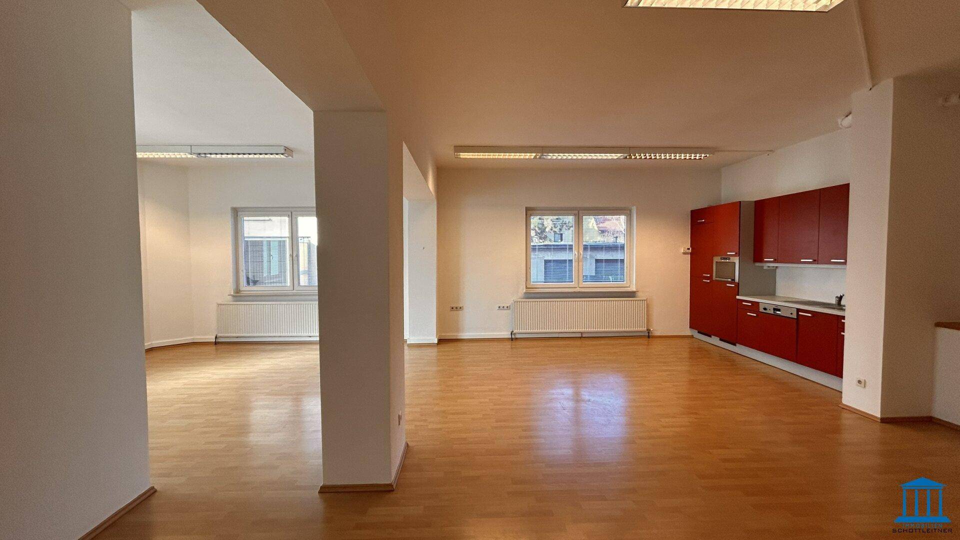 Geräumiger, offener Bürobereich mit integrierter roter Küchenzeile und hellem Holzfußboden.