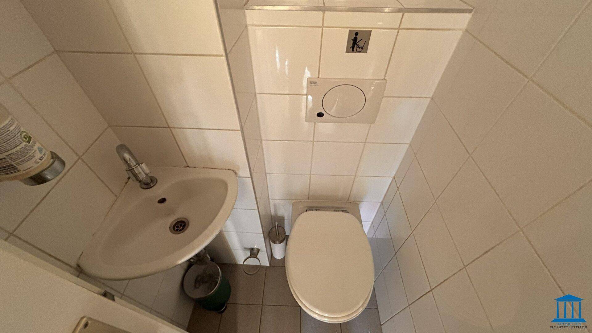 Kleine Gästetoilette mit weiß gefliesten Wänden, Waschbecken und WC.