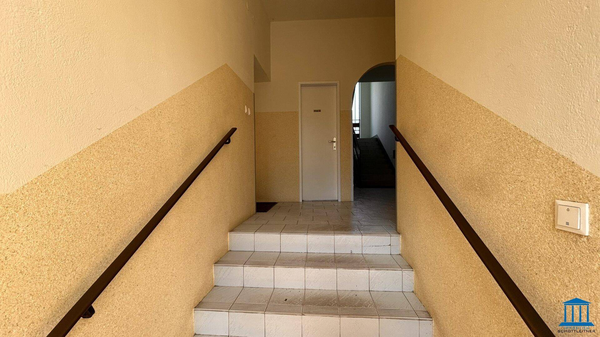 Treppenhaus mit Fliesenstufen, Handläufen und zweifarbigen Wänden in Beige und Weiß.