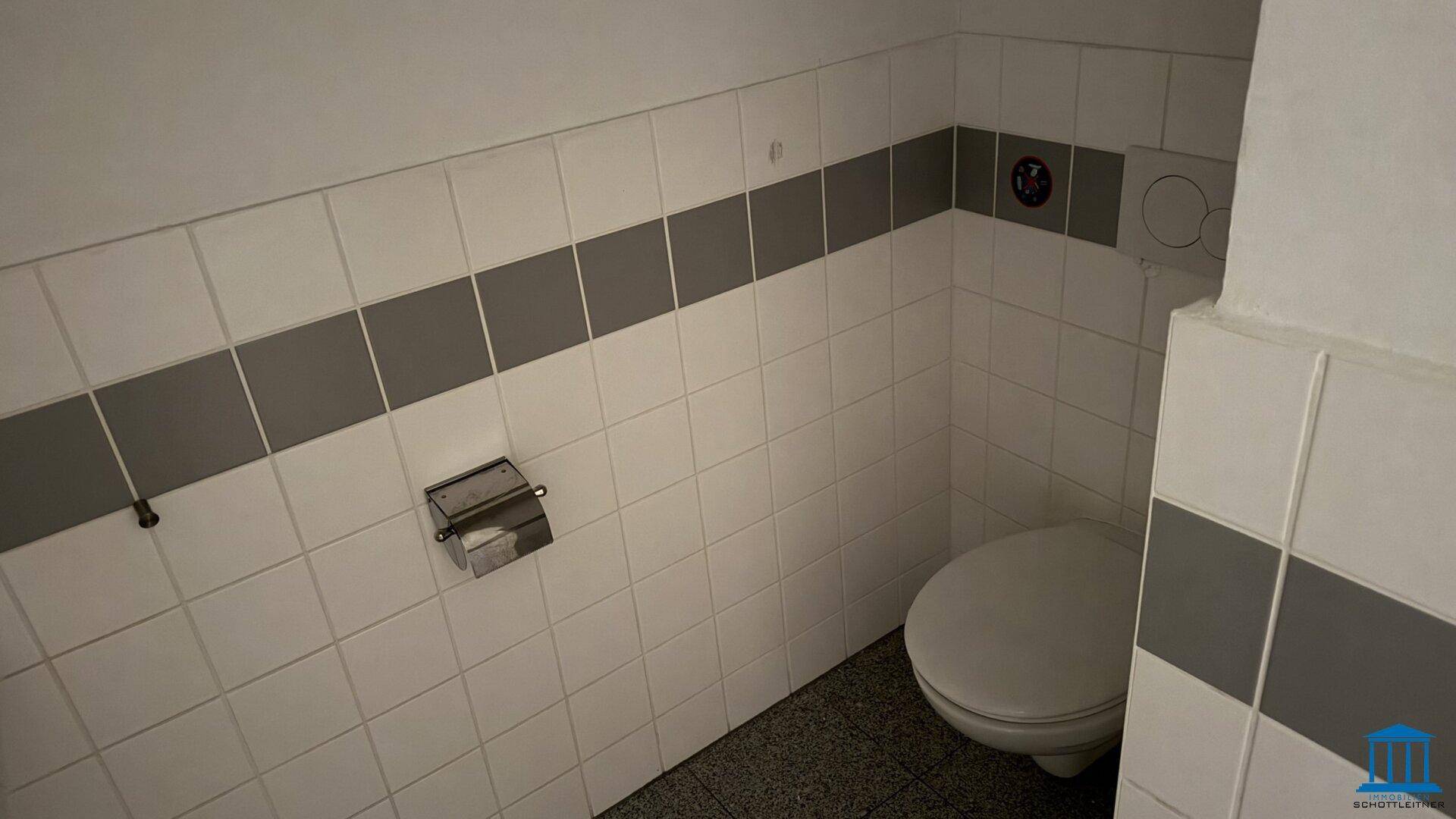 Funktionale Gästetoilette mit weißen und grauen Fliesen, sauber und gut gepflegt.
