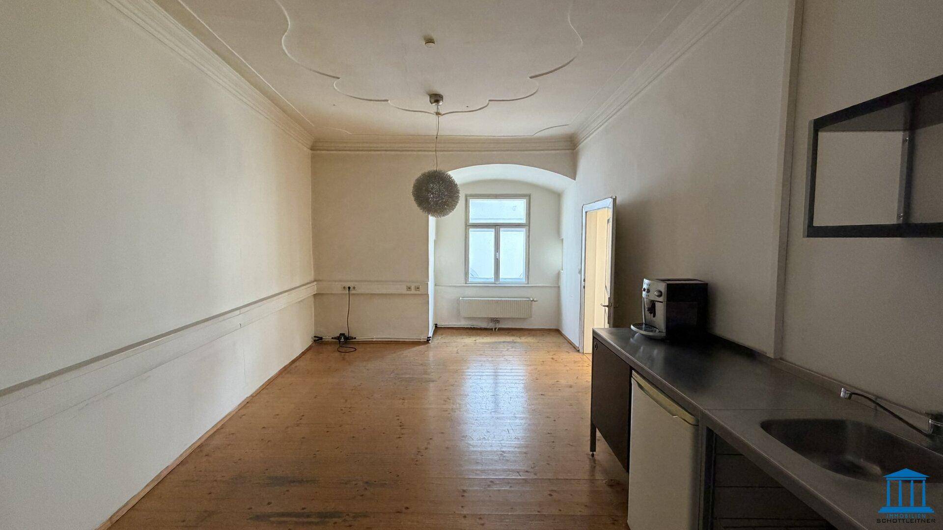 Büroraum mit integrierter kleiner Küchenzeile und dekorativer Deckenleuchte, ideal für Pausen.