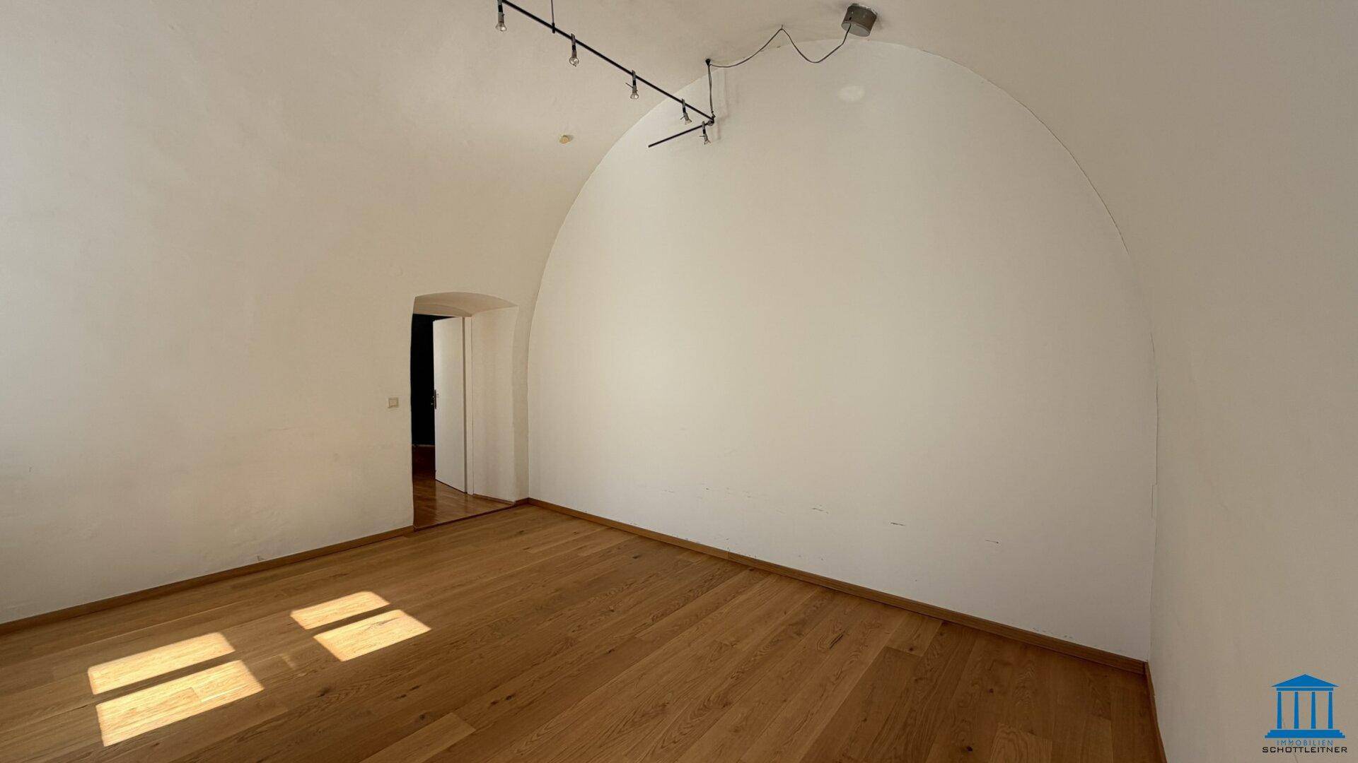 Geräumiger Raum mit gewölbter Decke und Holzboden, durchflutet von natürlichem Licht.