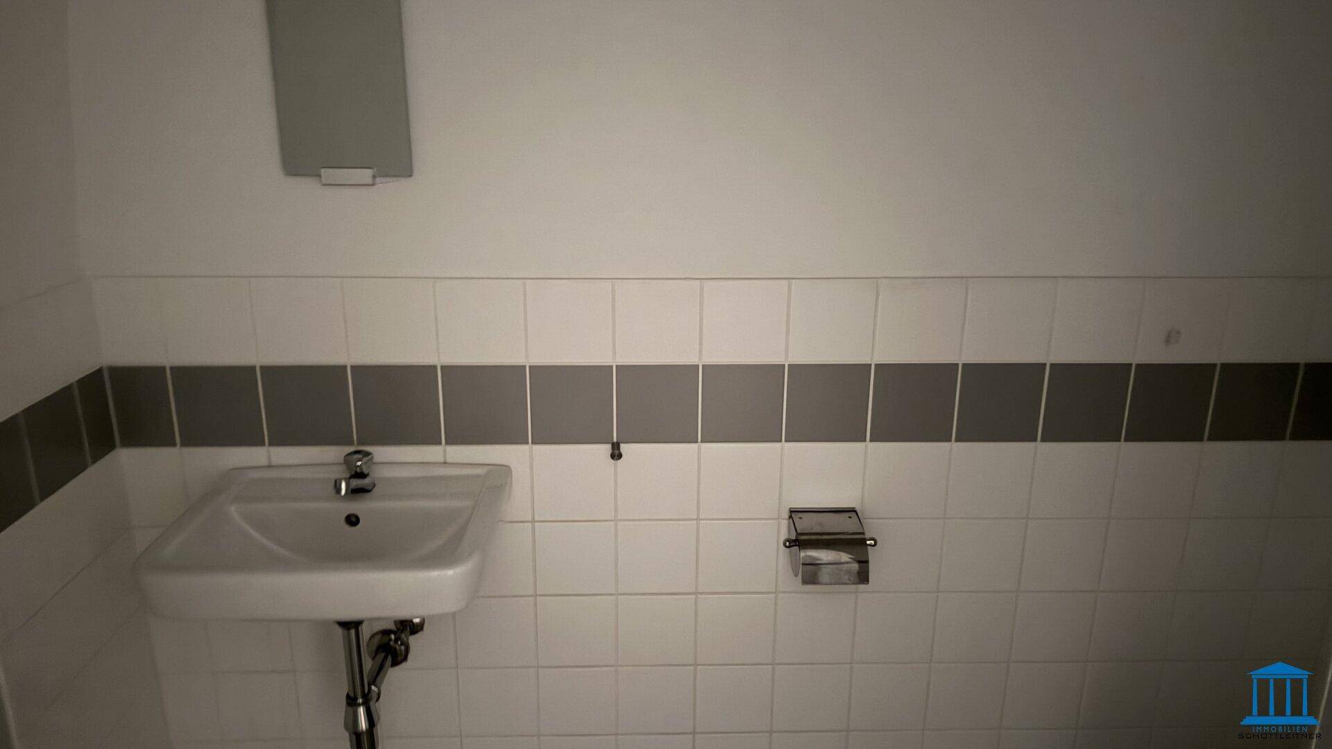 Schlichtes Waschbecken in einer Gästetoilette mit weißen und grauen Fliesen, praktisch und ordentlich.