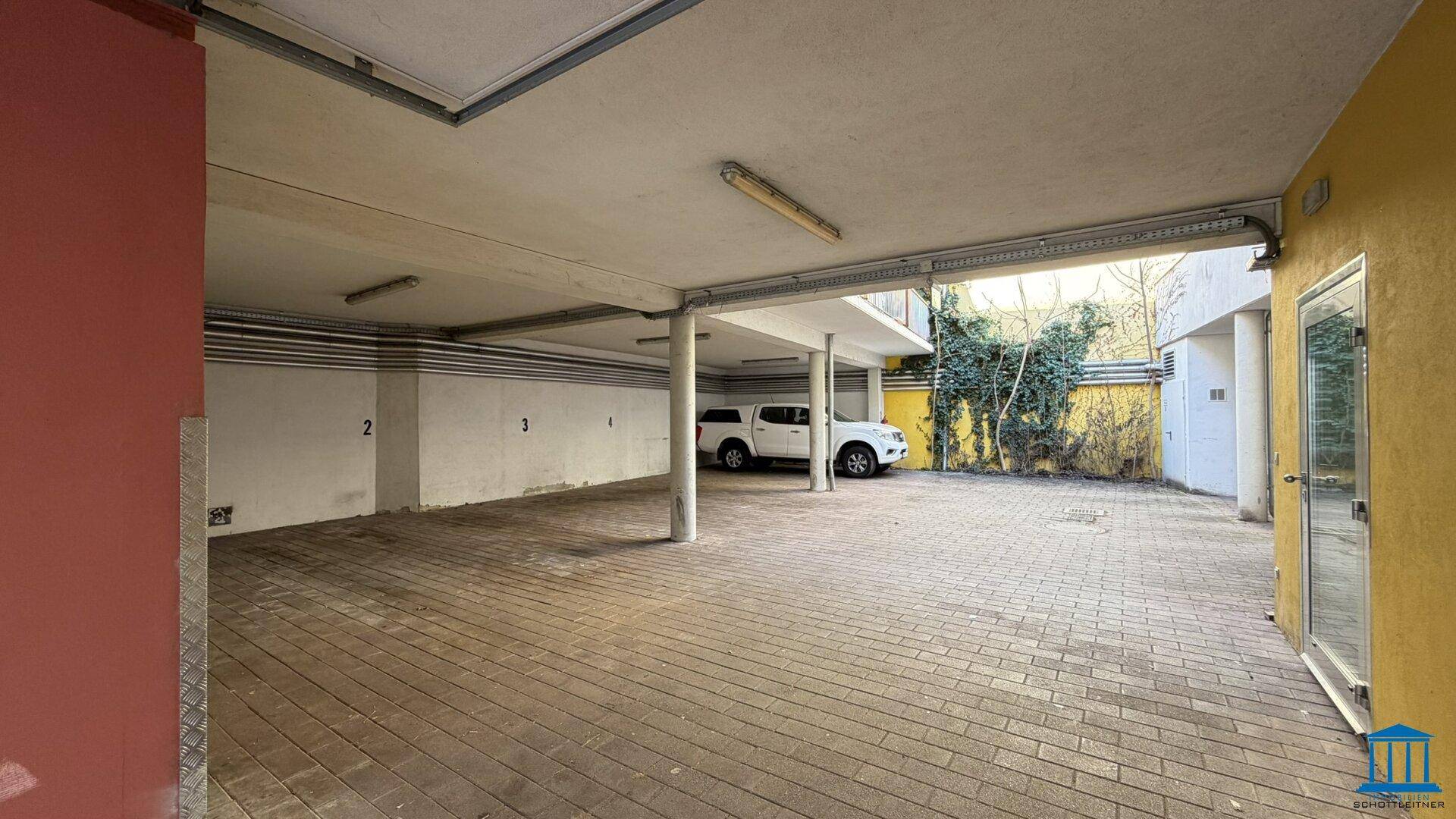 Überdachter Parkplatzbereich mit Pflastersteinen und Platz für mehrere Fahrzeuge.